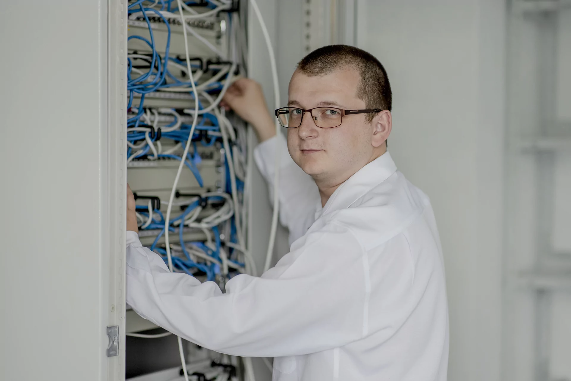 Ein Mann im wei&szlig;en Hemd arbeitet an einem Server-Schrank und passt Kabel an.