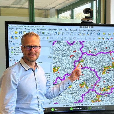 Ein Mann steht vor einem Bildschirm mit einer digitalen Karte und zeigt auf einen Punkt auf der Karte.