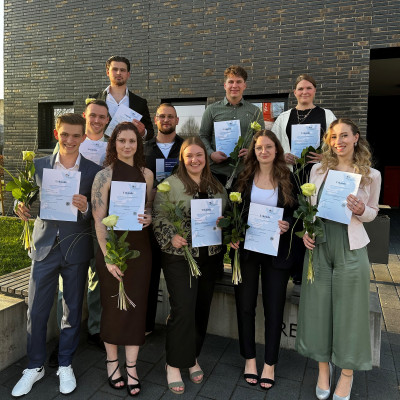 Absolventinnen und Absolventen halten ihre Urkunde und eine gelbe Rose in der Hand.