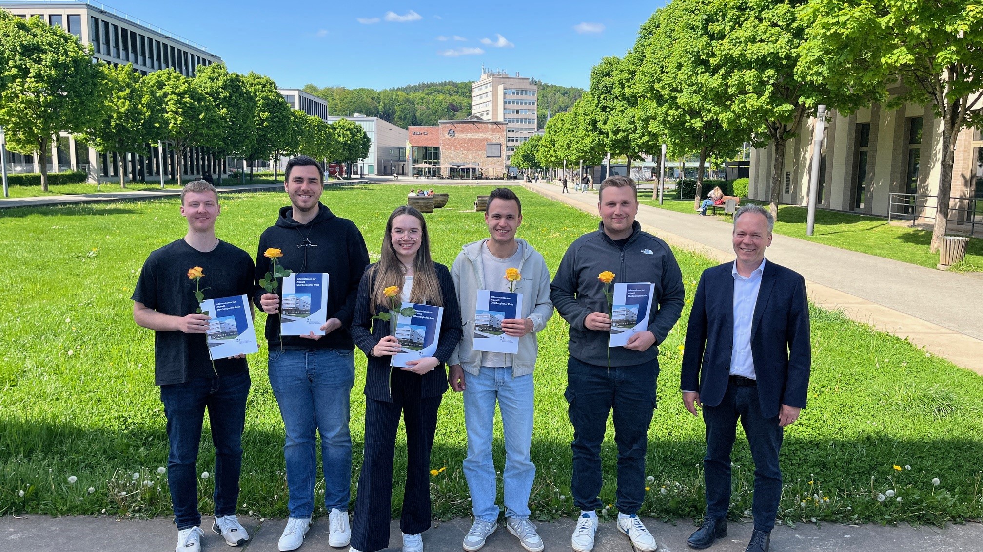 Absolventinnen und Absolventen halten ihre Urkunde und eine gelbe Rose in der Hand.